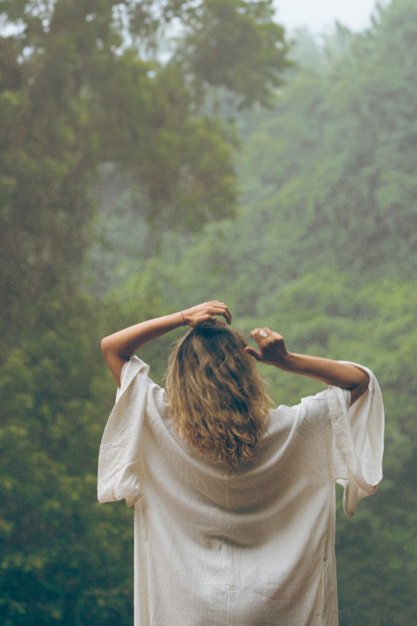 A woman standing in the rainforest combing her hair with her hands. 